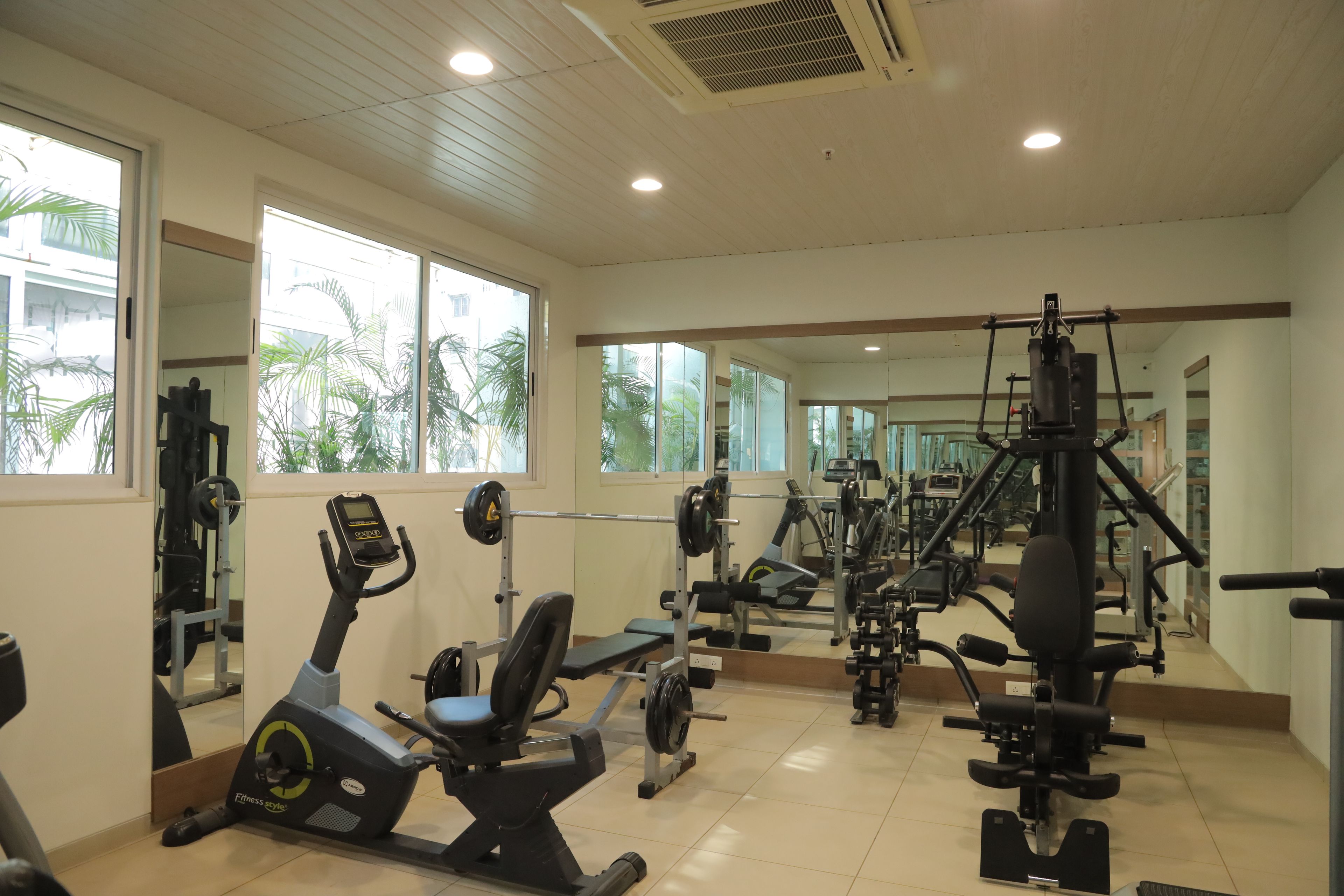 A gym with various exercise equipment, large windows, and a mirrored wall.