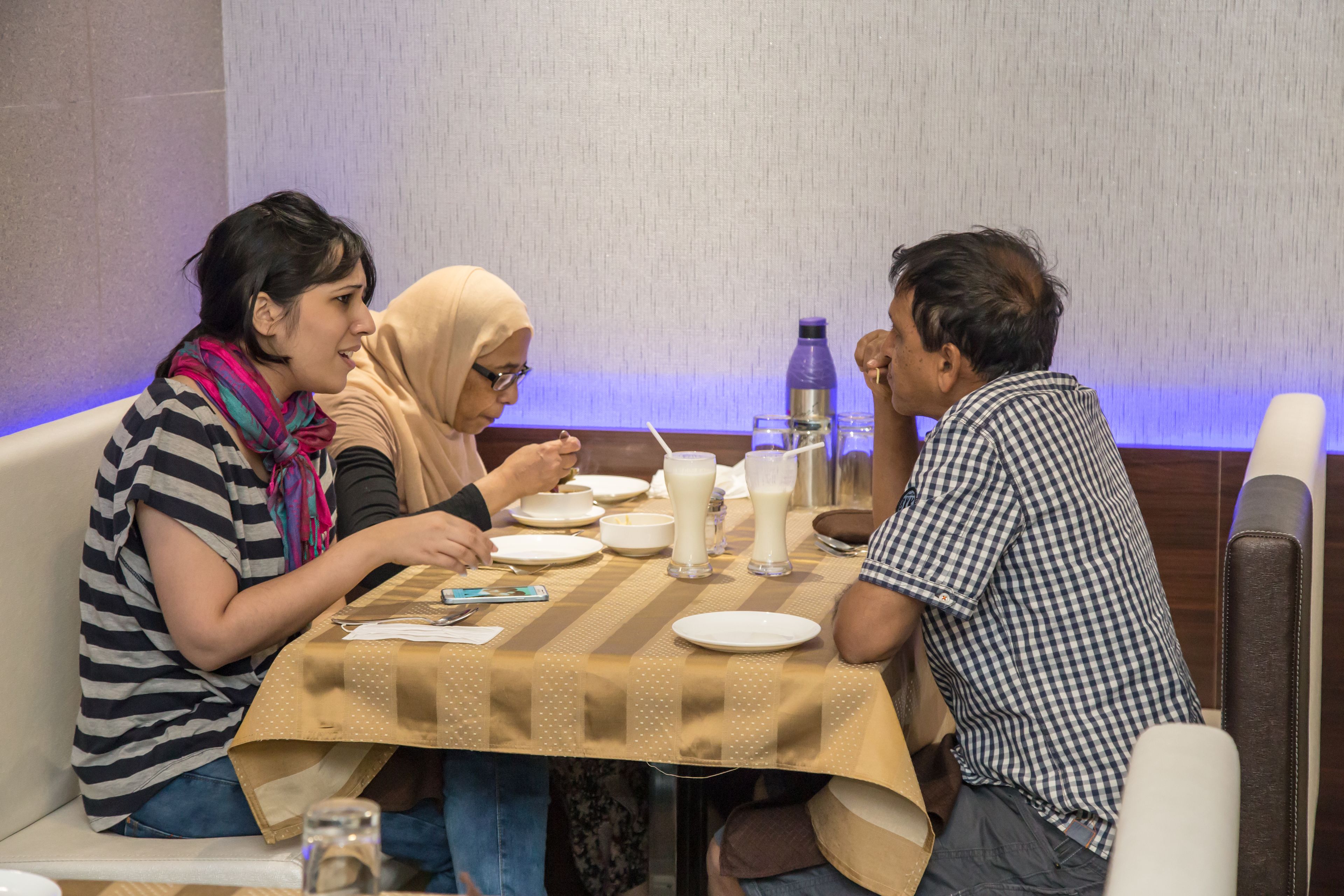 A group of people dining at a table with a striped tablecloth, white plates, and a water bottle.