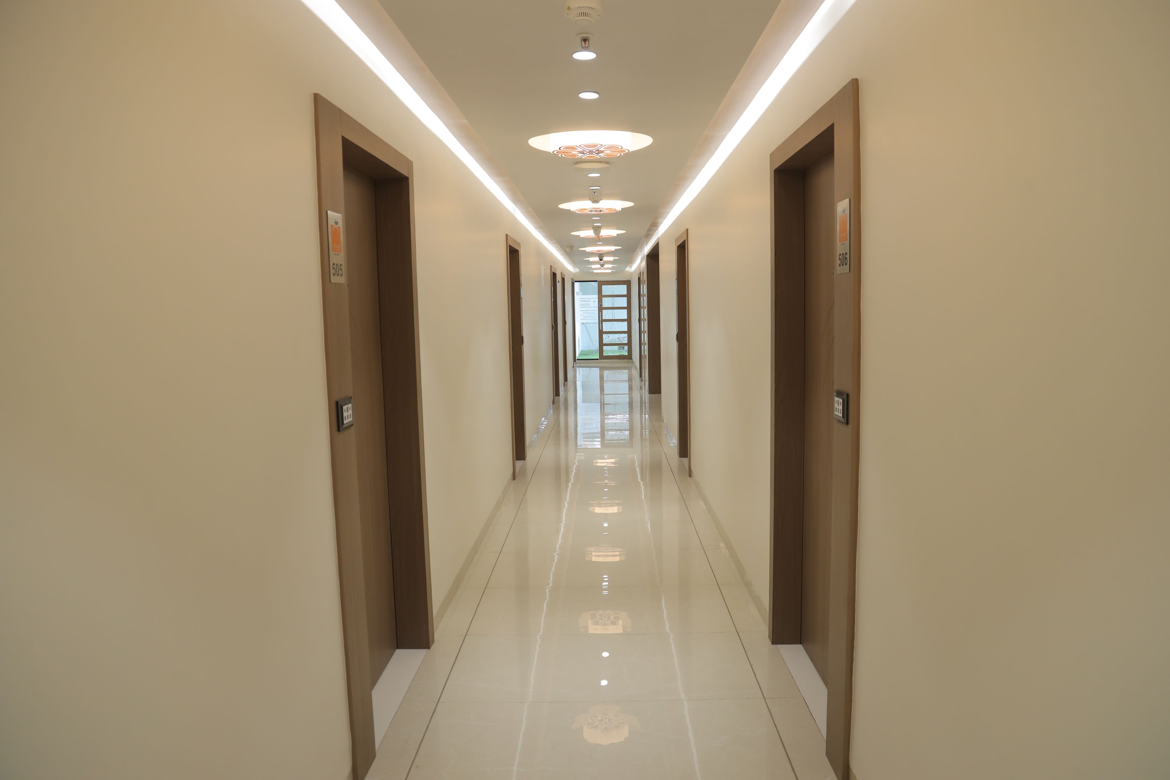 A long, narrow hallway with doors on both sides, recessed lighting, and a shiny tiled floor.
