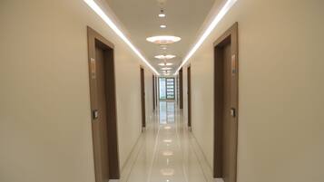 A long, narrow hallway with doors on both sides, recessed lighting, and a shiny tiled floor.