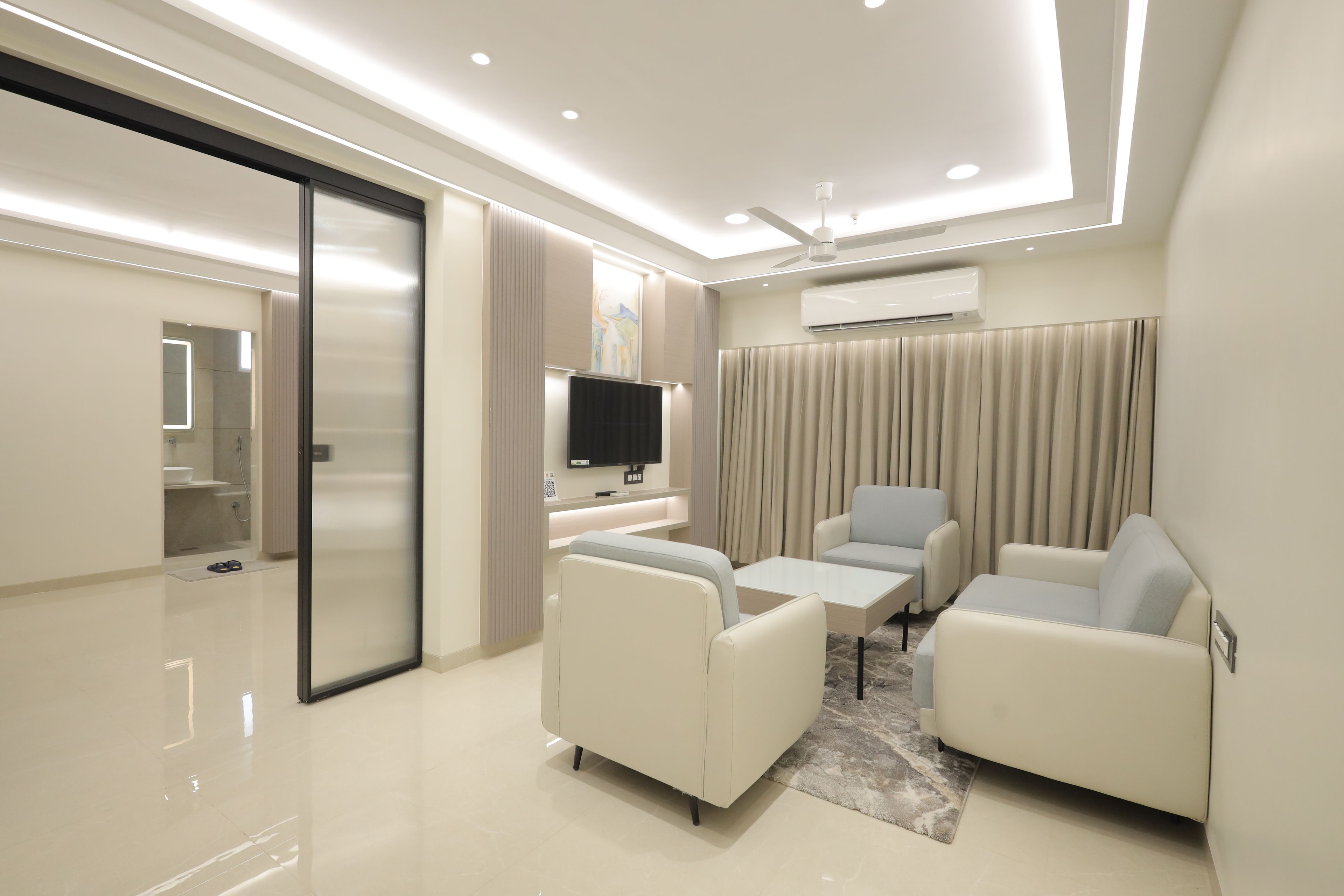 Une chambre d’hôtel moderne équipée d’un téléviseur à écran plat, de deux canapés, d’une table basse et d’un ventilateur de plafond.