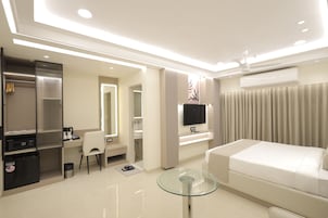 Habitación de hotel moderna con cama, escritorio, silla, mesa de vidrio, armario y televisor.