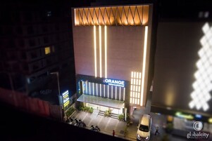 Un hotel con fachada moderna, un llamativo letrero de 'ORANGE International' y un estacionamiento con vehículos.