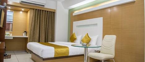 A hotel room with a bed, a glass table, a chair, a ceiling fan, and a wall-mounted air conditioner.