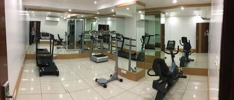 Une salle de sport équipée de divers appareils d’exercice, notamment des tapis de course, des vélos d’appartement et des appareils de musculation.