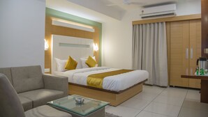 A modern hotel room with a large bed, a sofa, a glass coffee table, and a wardrobe. - Hotel Orange International (Surat)