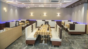 A restaurant with a long table, booths, and a marble floor. - Hotel Orange International (Surat)
