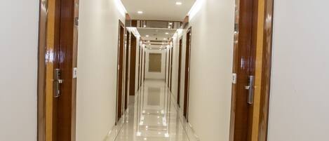 A long, well-lit hallway with wooden doors on either side and a shiny tiled floor.