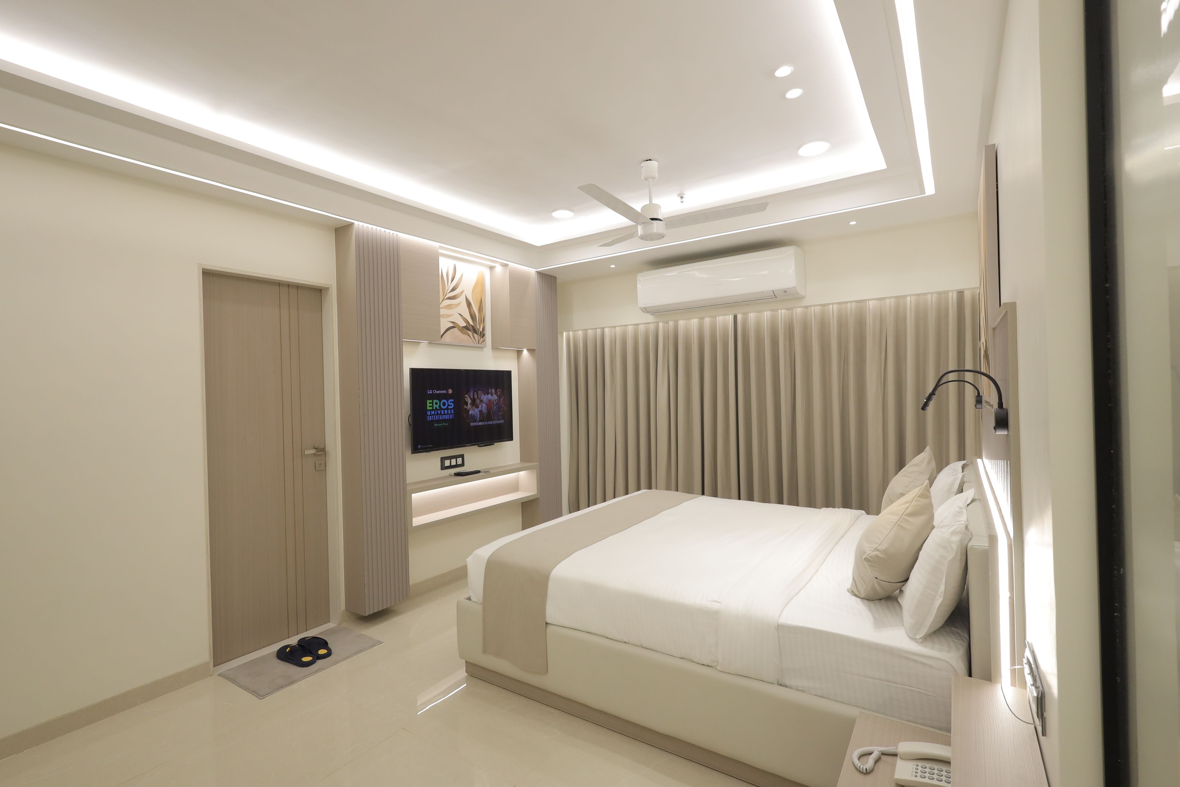 A modern bedroom with a bed, a TV, an air conditioning unit, and a ceiling fan.