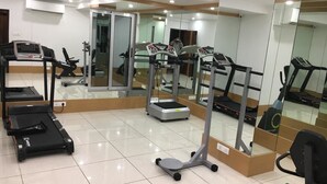 A gym with treadmills, elliptical machines, and weight stations. - Hotel Orange International (Surat)