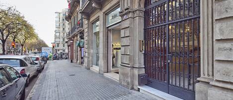 A cobblestone street lined with parked cars and historic buildings with ornate iron gates.