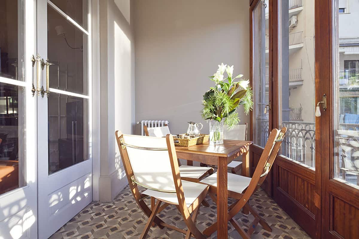 Une pièce baignée de lumière, avec une table et des chaises en bois, un vase rempli de fleurs et une vue sur la rue par la fenêtre.