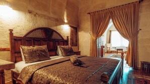 A spacious bedroom with a large bed, wooden headboard, and a view of a balcony. - Melis Cave Hotel (Ürgüp)