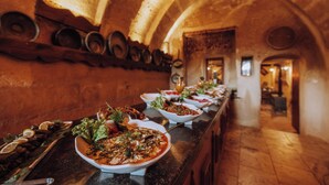 A long table with various dishes, a rustic brick wall, and an arched ceiling. - Melis Cave Hotel (Ürgüp)