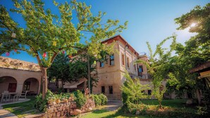A courtyard with a stone wall, a tree, and a building with a balcony. - Melis Cave Hotel (Ürgüp)