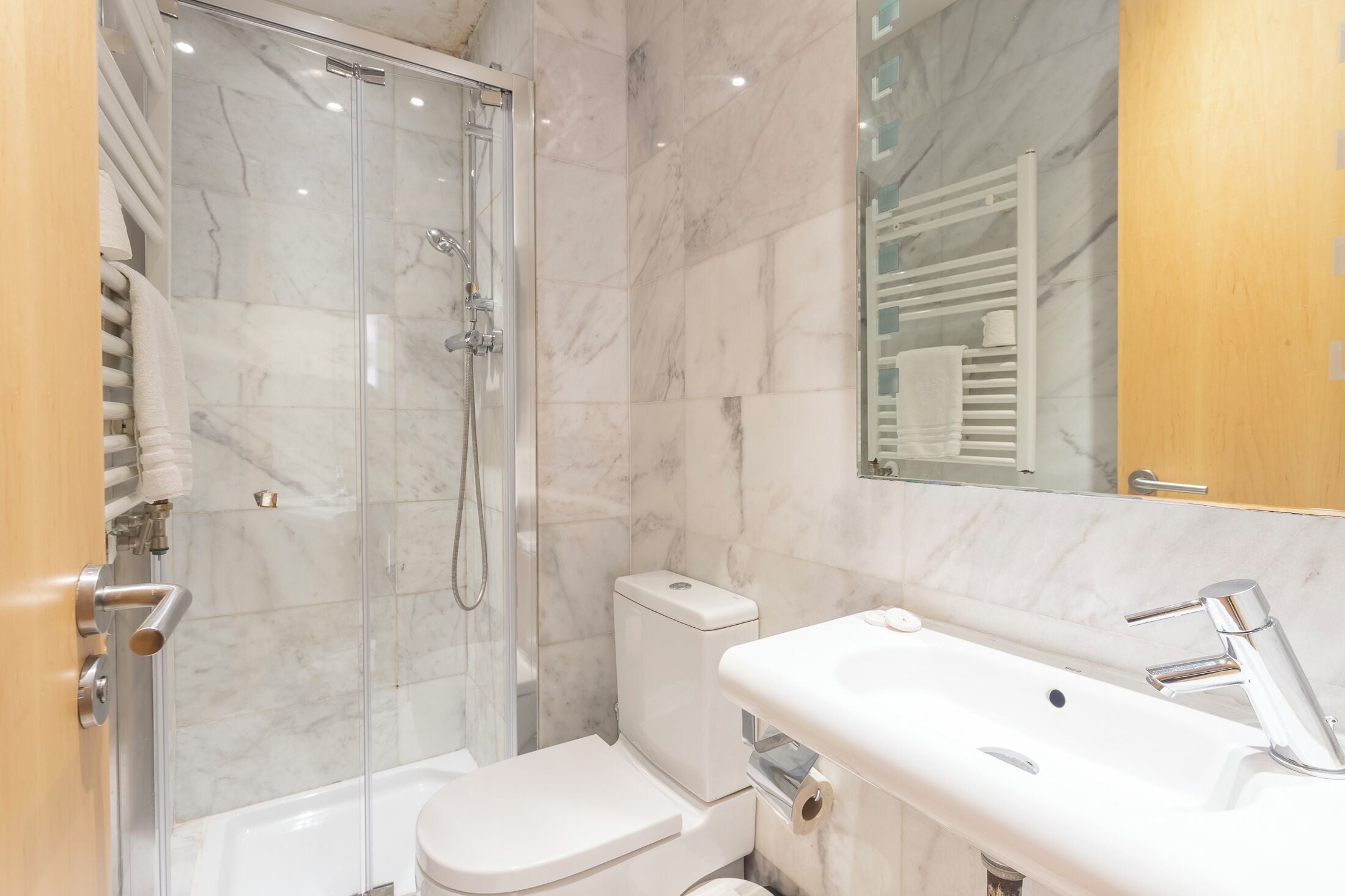 A modern bathroom with a glass-enclosed shower, a white toilet, and a sink with a chrome faucet.