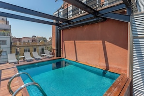 A rooftop pool with clear blue water, surrounded by wooden deck and lounge chairs.