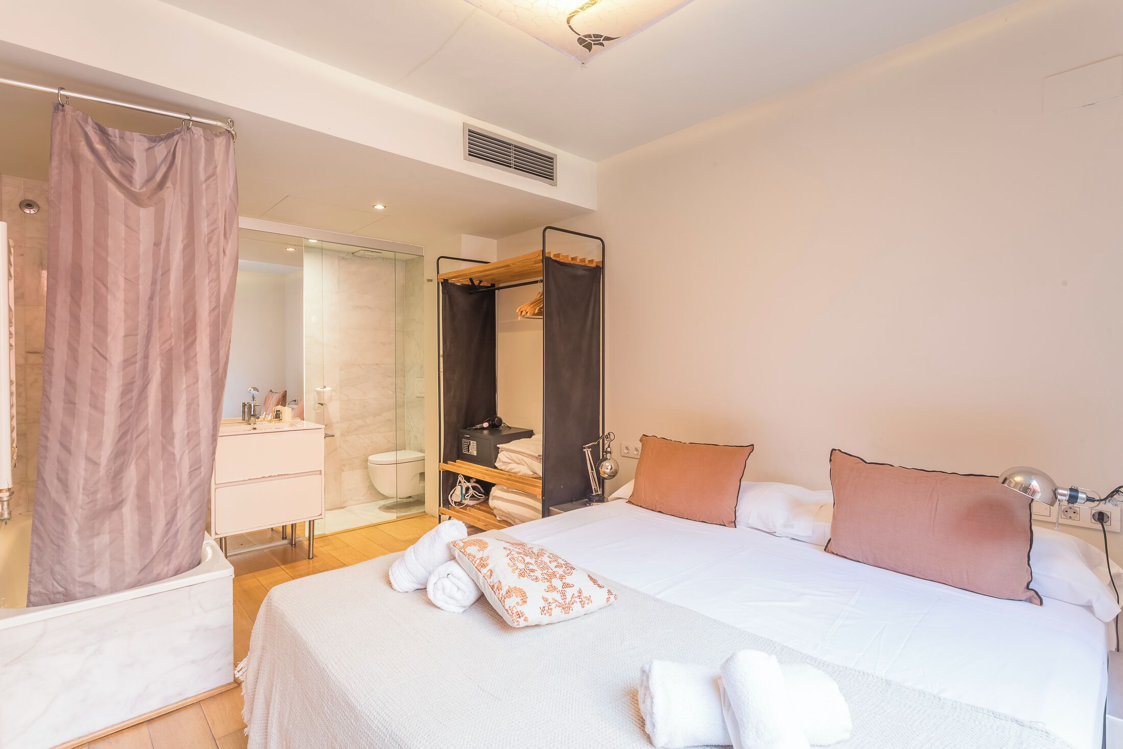 A modern hotel room with a large bed, a walk-in closet, a glass shower, and a bathroom with a white sink and mirror.