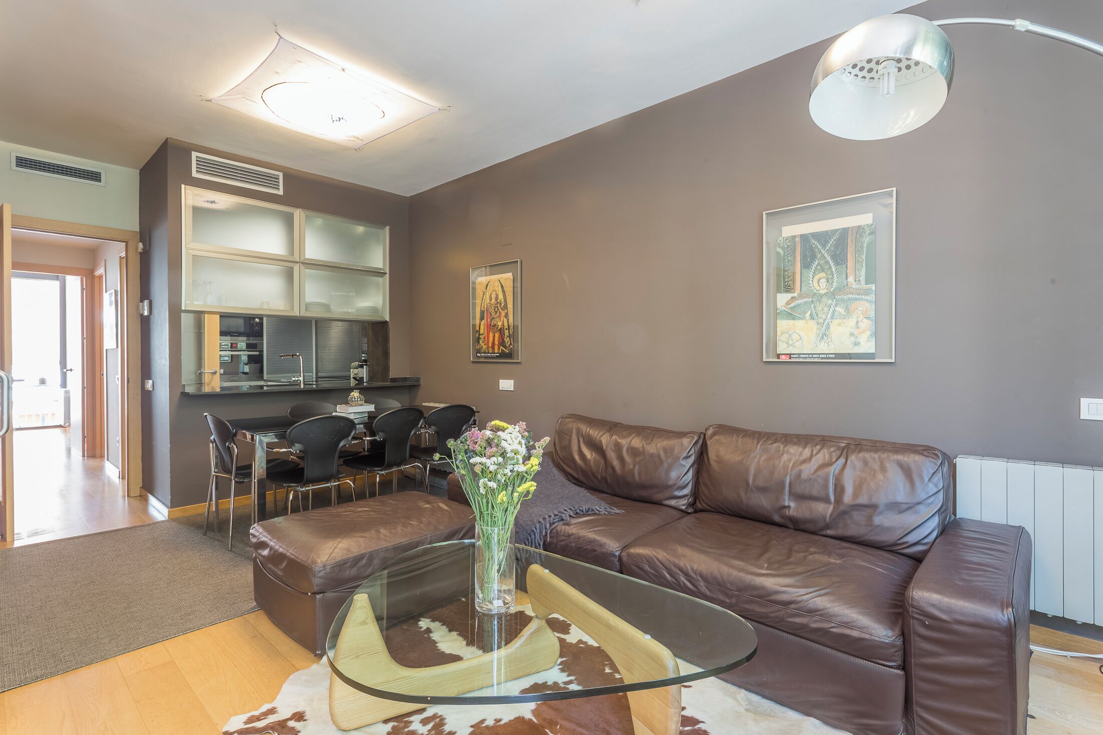 Una sala moderna con una mesa de centro de vidrio, sofá de cuero y una zona de comedor con sillas.