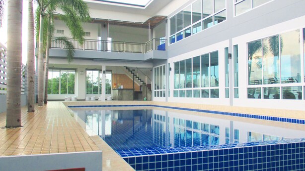 Una piscina interior moderna con suelo de baldosas, ventanas amplias y una escalera que sube a un nivel superior.