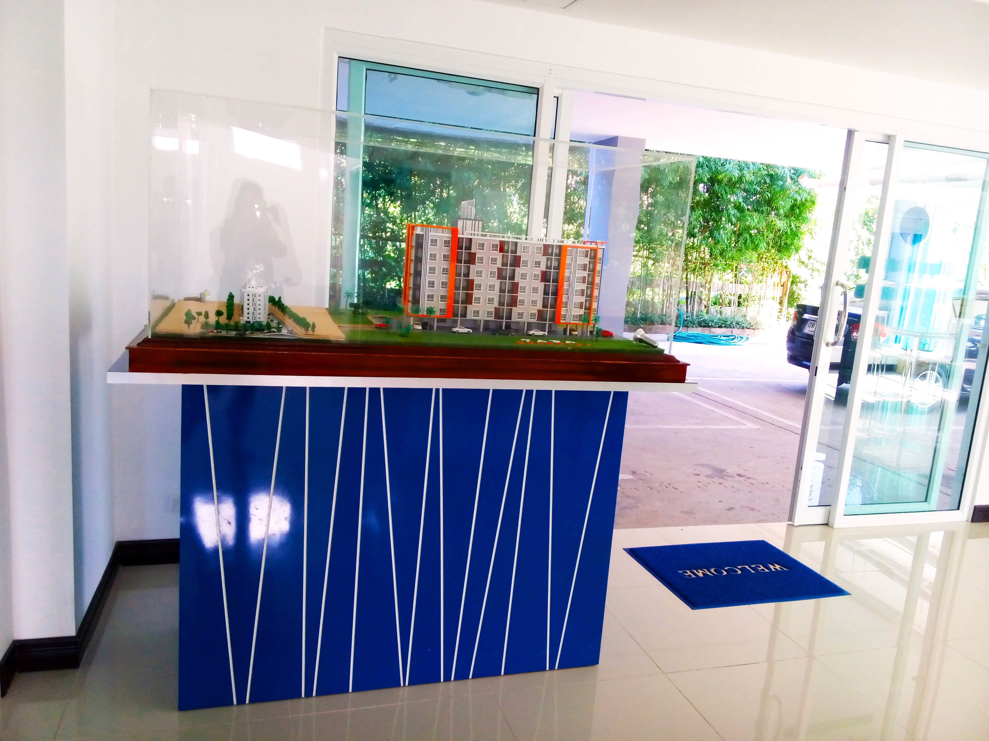 A reception desk with a model of a building, a glass door, and a blue mat on the floor.