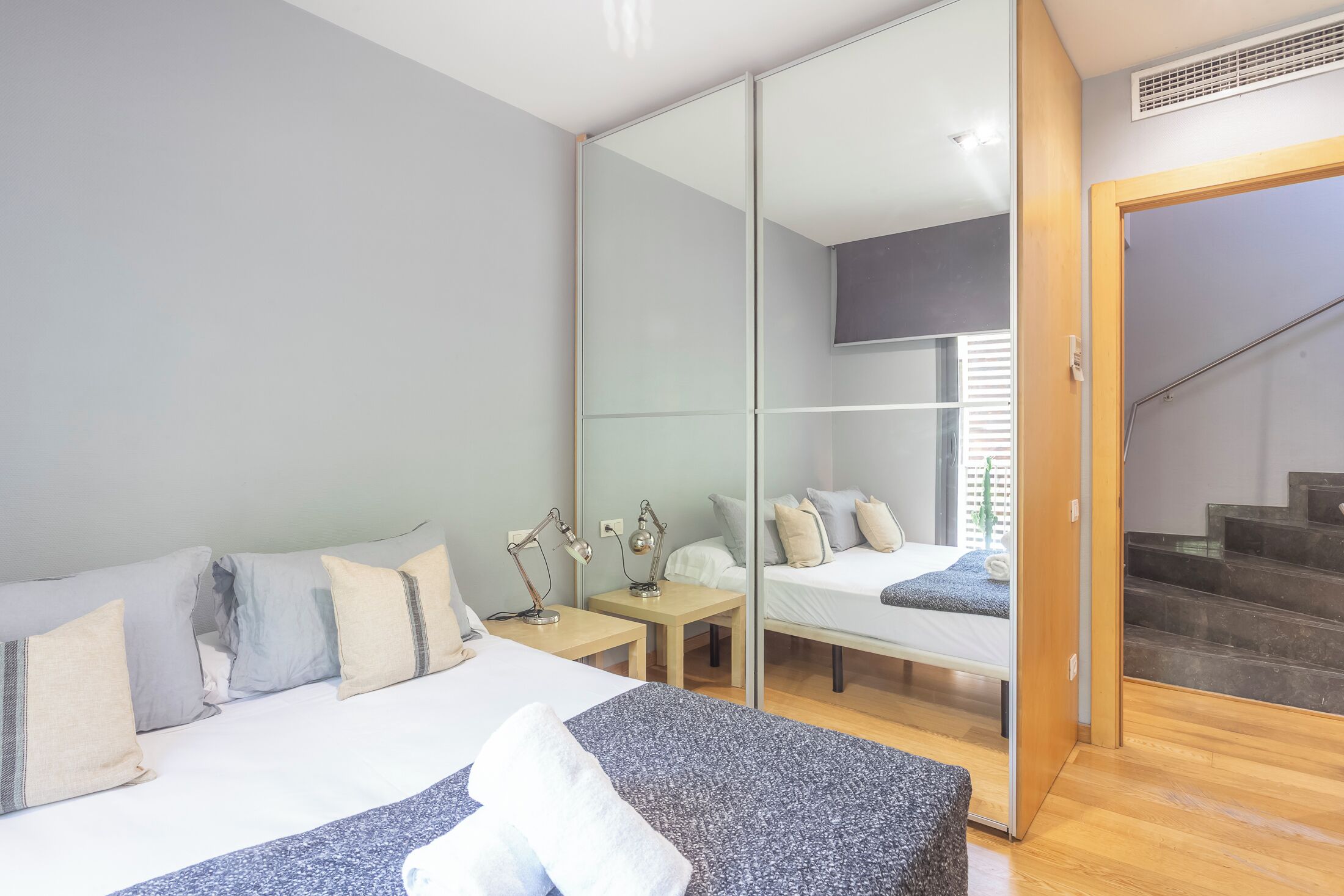 Ein modernes Schlafzimmer mit einem großen Bett, Nachttischen, einem Spiegel und einer Treppe.