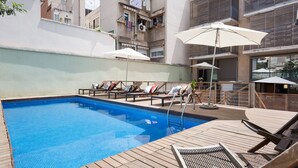 A rooftop pool with lounge chairs and umbrellas, surrounded by buildings.