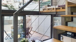 A modern interior with a staircase, a dining area with a table and chairs, and a view through large windows.