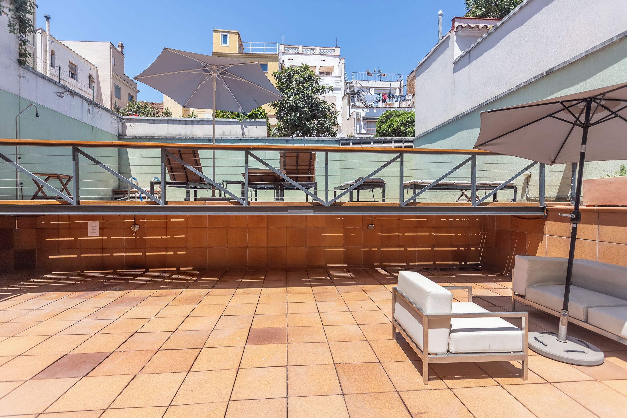 An outdoor patio with tiled flooring, wooden furniture, and umbrellas.