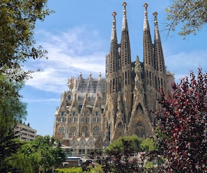 Experience the iconic Sagrada Familia, featuring Antoni Gaudí's distinctive spires and intricate facade amidst lush surroundings.