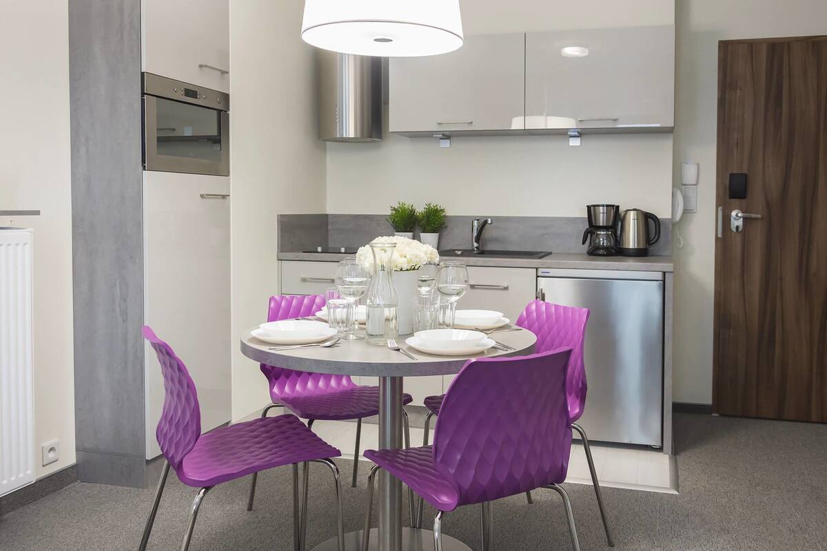 A modern kitchen with stainless steel appliances, a dining area with purple chairs, and a round table set for four.