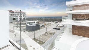 A modern building with a glass facade overlooking a parking area and a view of the sea. - VacationClub - Baltic Park Molo Apartments (Swinoujscie)