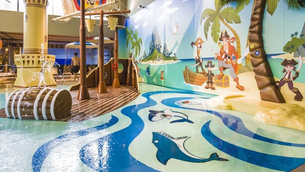 An indoor water play area with a pirate theme, including a ship, palm trees, and sea creatures. - VacationClub - Baltic Park Molo Apartments (Swinoujscie)