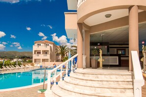 A hotel pool area with a clear blue sky, a pool, and a staircase leading to the entrance.