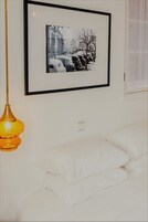 Fotografía en blanco y negro, enmarco, muestra una escena callejera con autos antiguos y edificios, colgada sobre una cama con ropa blanca.