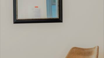 A chair with a woven backrest and wooden legs, positioned against a plain wall with a framed certificate or document hanging above it.