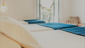 A bedroom with two beds, a chair, a desk, and a window with a view of greenery. - Comercial Boutique Azores (Ponta Delgada)