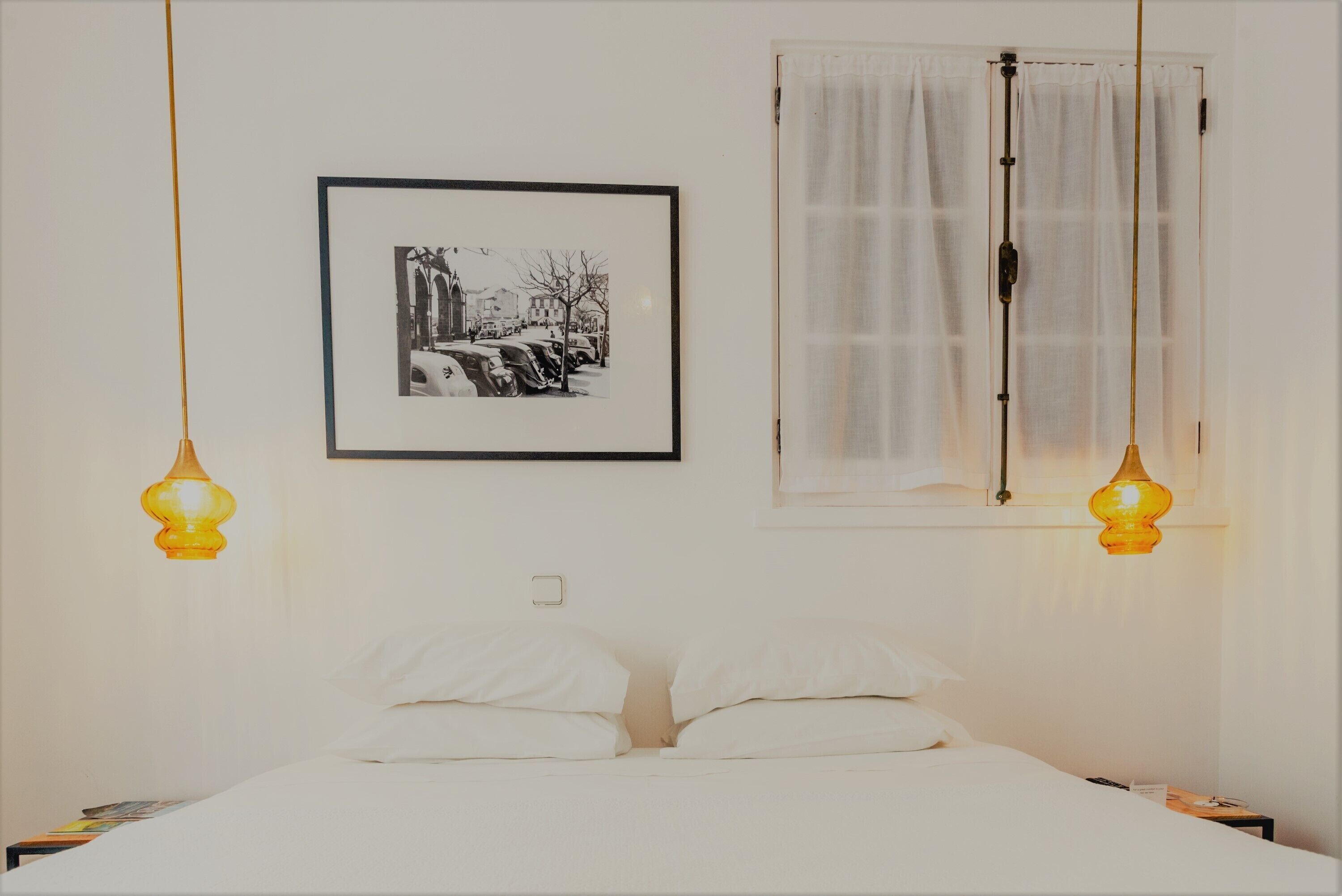 A bed with white linens, a framed black and white photo, and two hanging lamps.