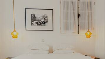 A bed with white linens, a framed black and white photo, and two hanging lamps.