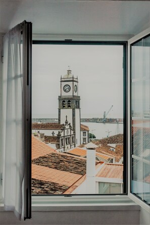Vista a través de una ventana que muestra un edificio con una torre de reloj, un puente y una masa de agua.