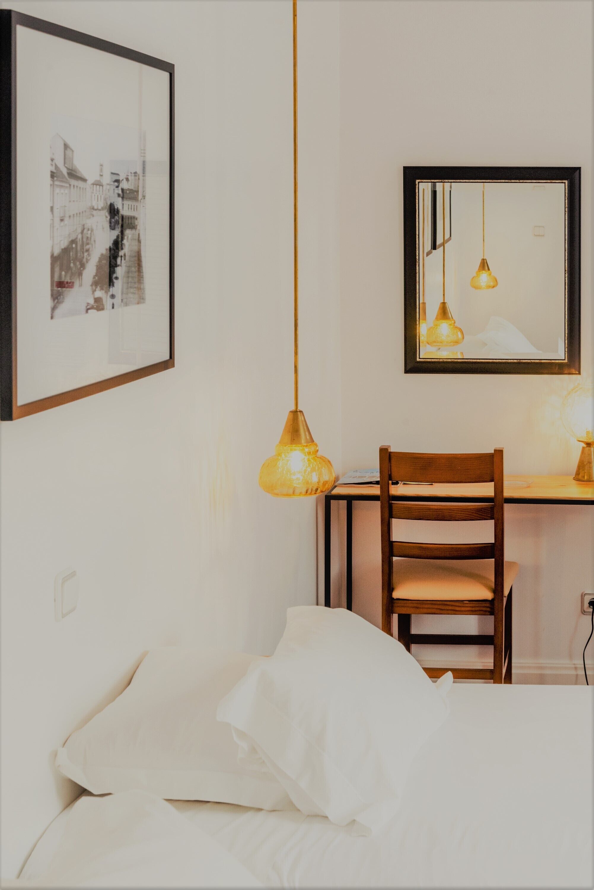 A bedroom with a bed, a desk, a chair, and a hanging light fixture.