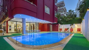 An indoor swimming pool with a clear blue water surface, surrounded by artificial green turf and a red building facade. - Twin Apart Hotel (Alanya)