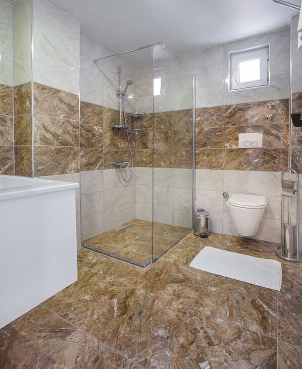 A modern bathroom with a glass-enclosed shower, a white bathtub, and a toilet. - Twin Apart Hotel (Alanya)