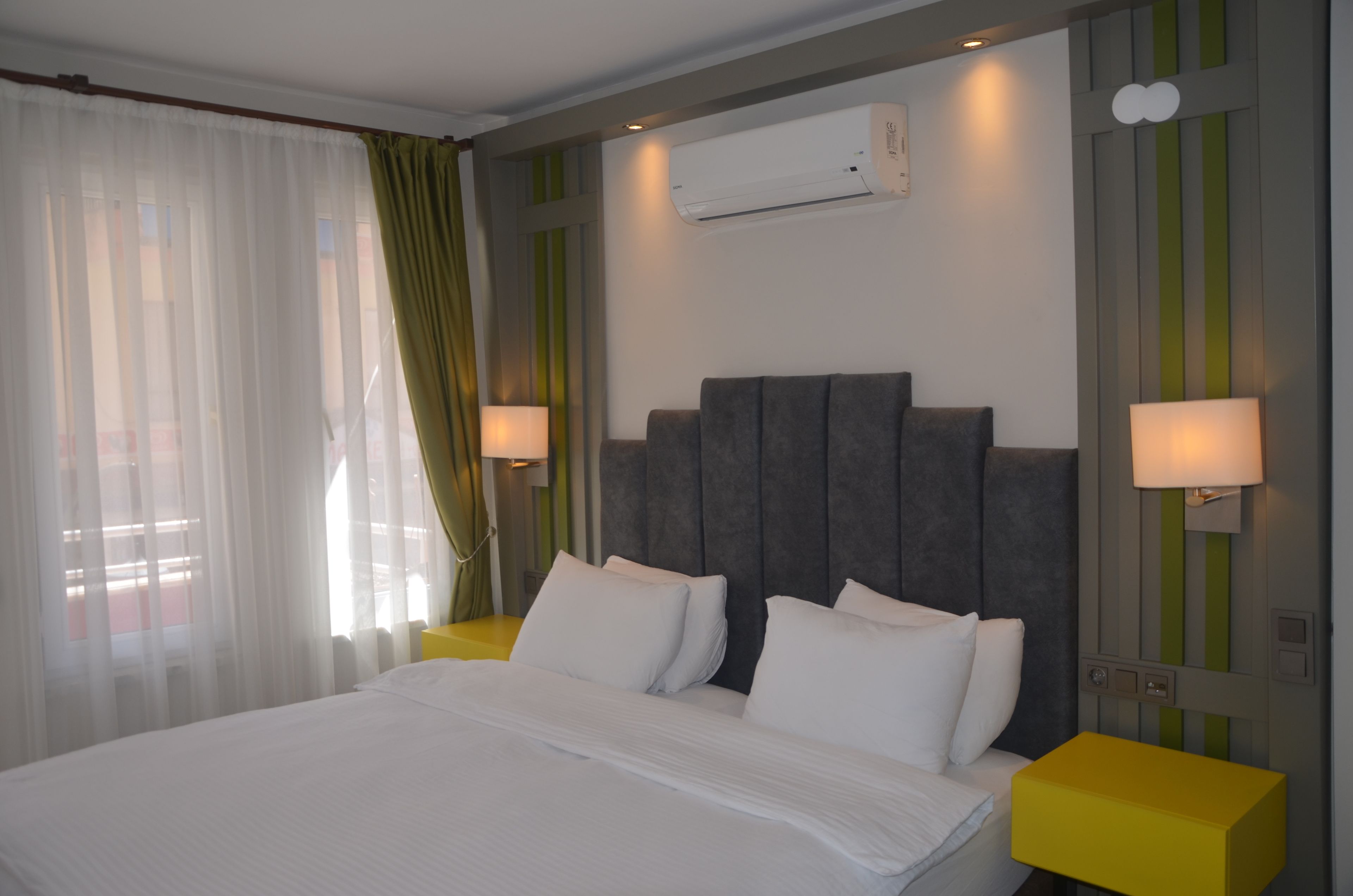 Una camera d'albergo con un letto grande, un comodino, un condizionatore d'aria e una finestra con tende.