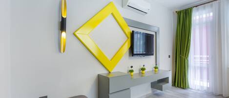 A modern living room with a grey sofa, a yellow decorative piece, a grey console table, a flat-screen TV, and a green curtain.