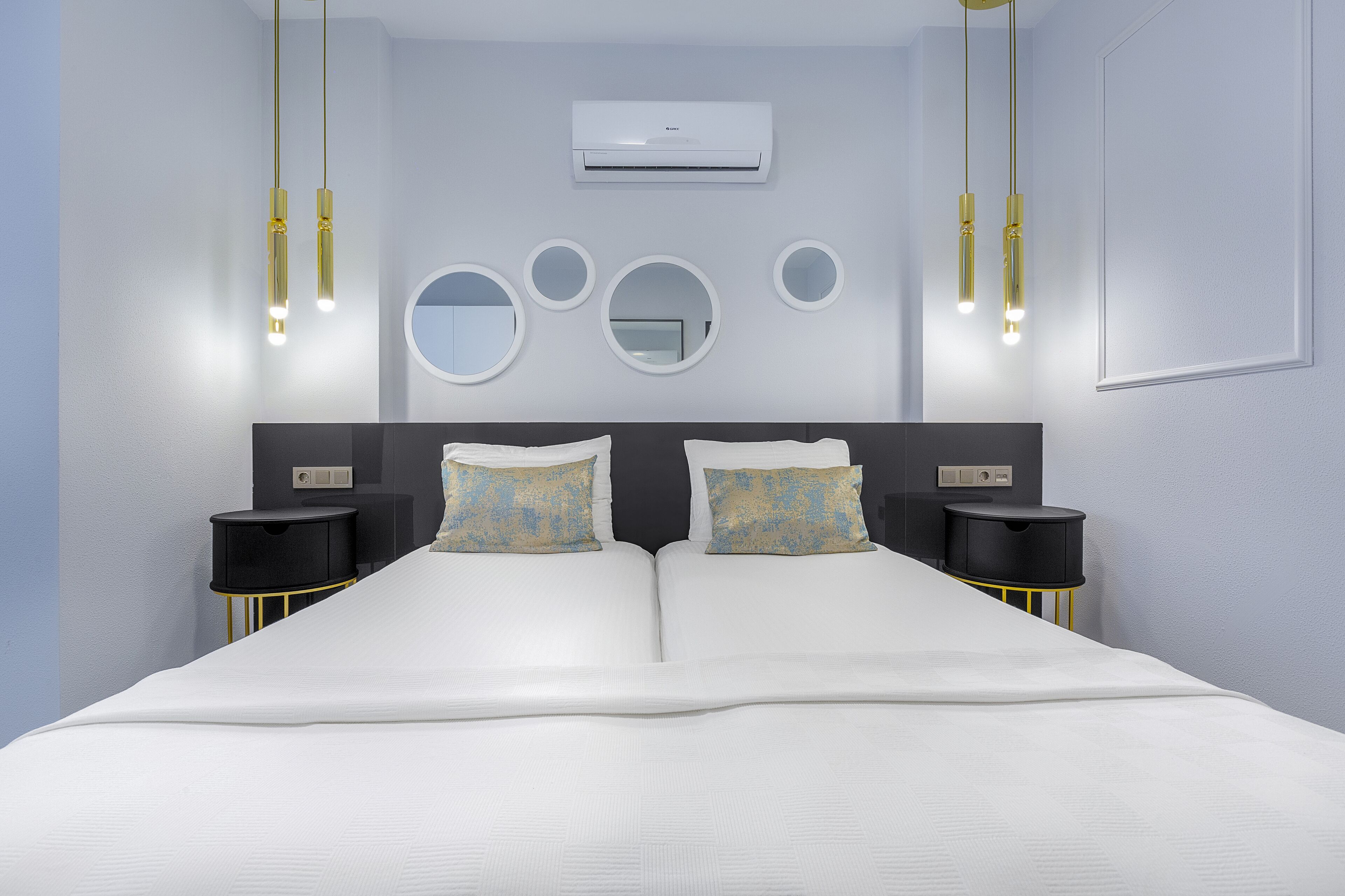 A modern bedroom with a large bed, two bedside tables, and a wall-mounted air conditioner.