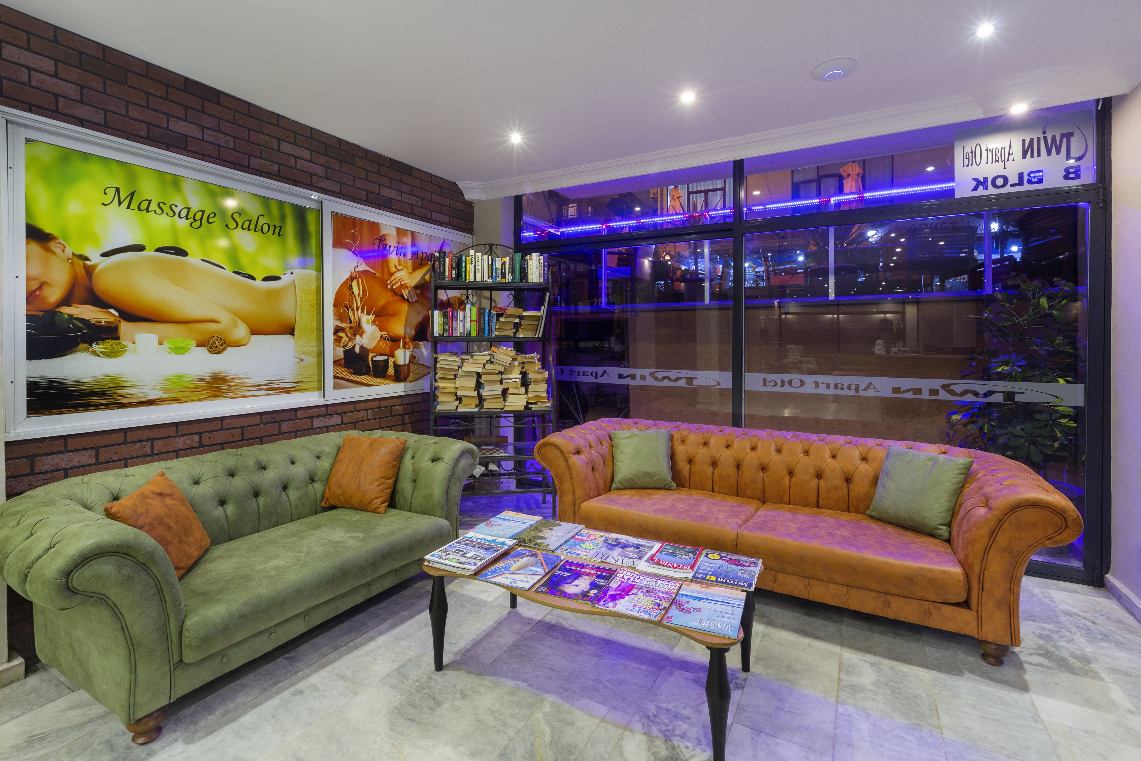A massage salon with a green and orange sofa, a coffee table with magazines, and a bookshelf.