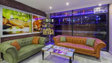 A massage salon with a green and orange sofa, a coffee table with magazines, and a bookshelf.