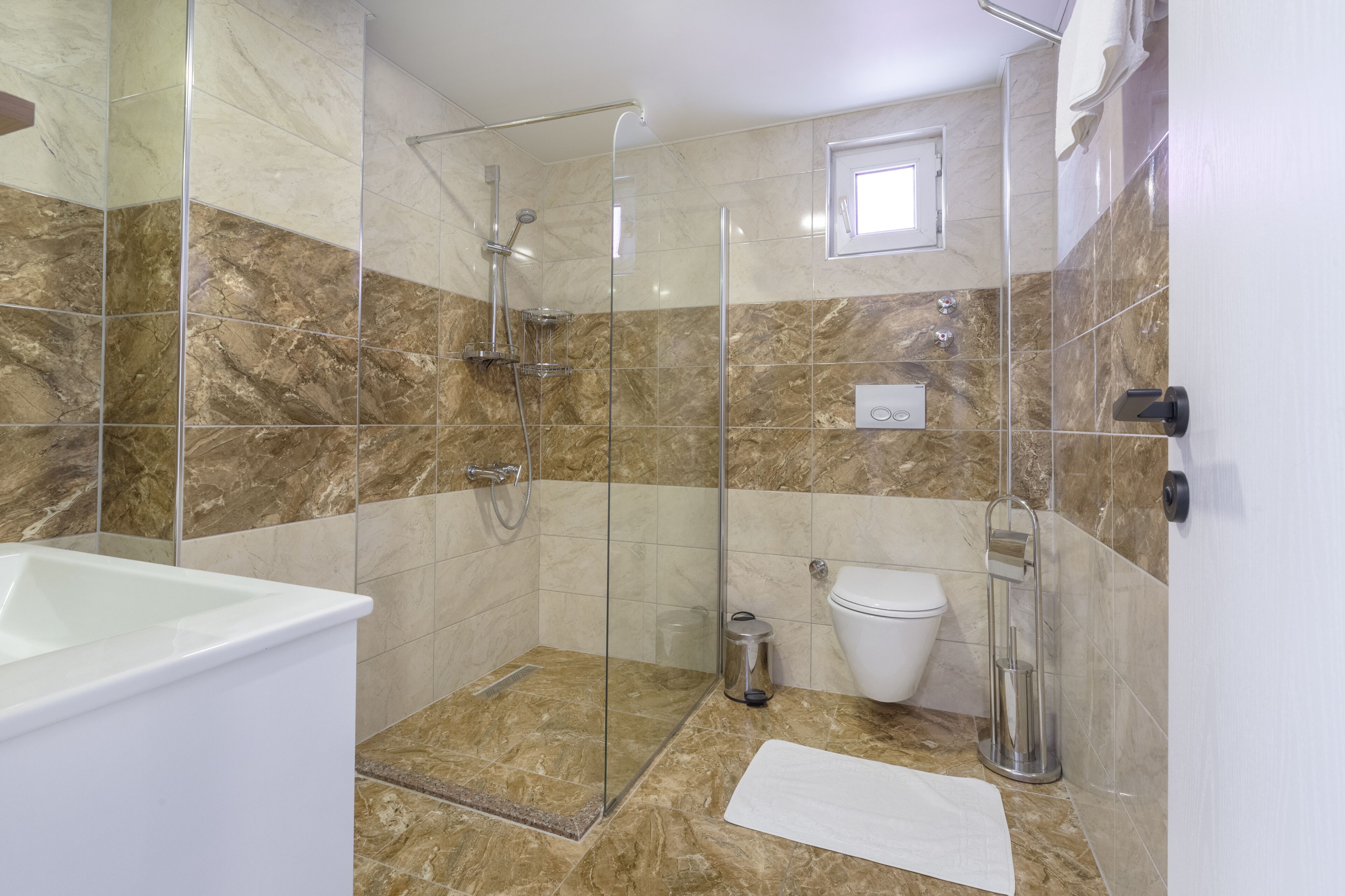 A bathroom with a glass-enclosed shower, a white bathtub, a toilet, and a marble-tiled floor.