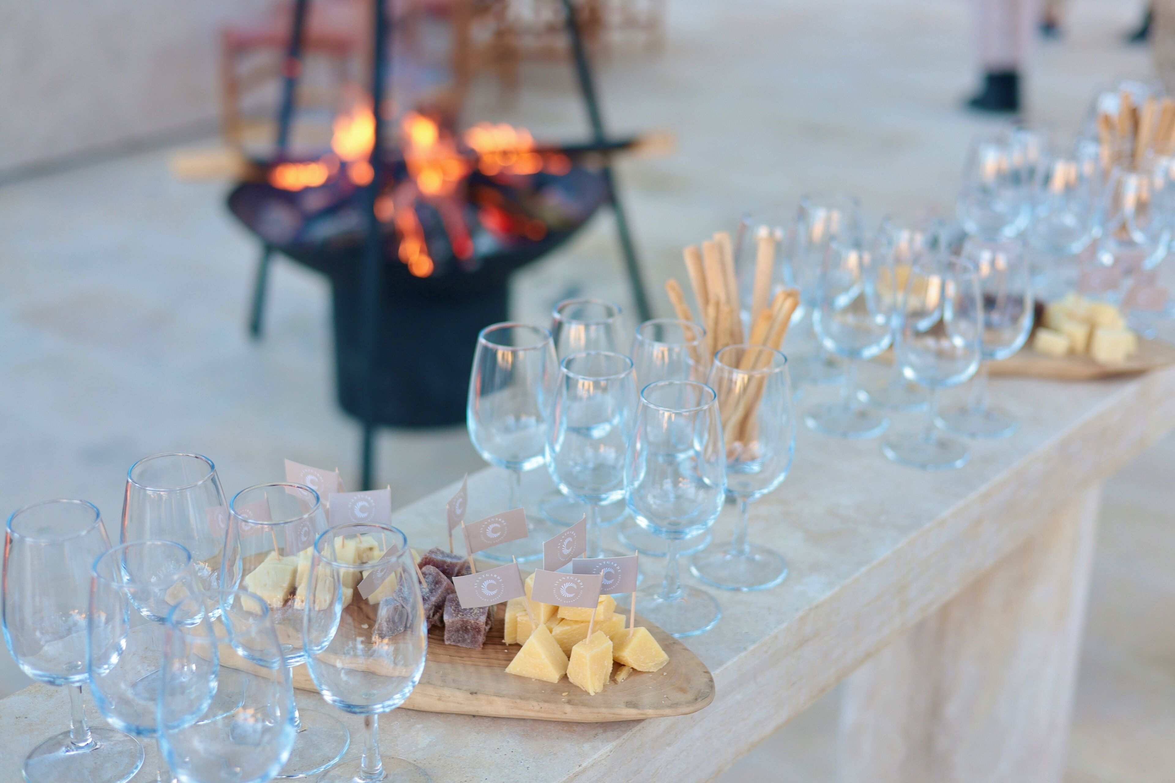 Una larga mesa con copas de vino y queso, dispuesta para una reunión.